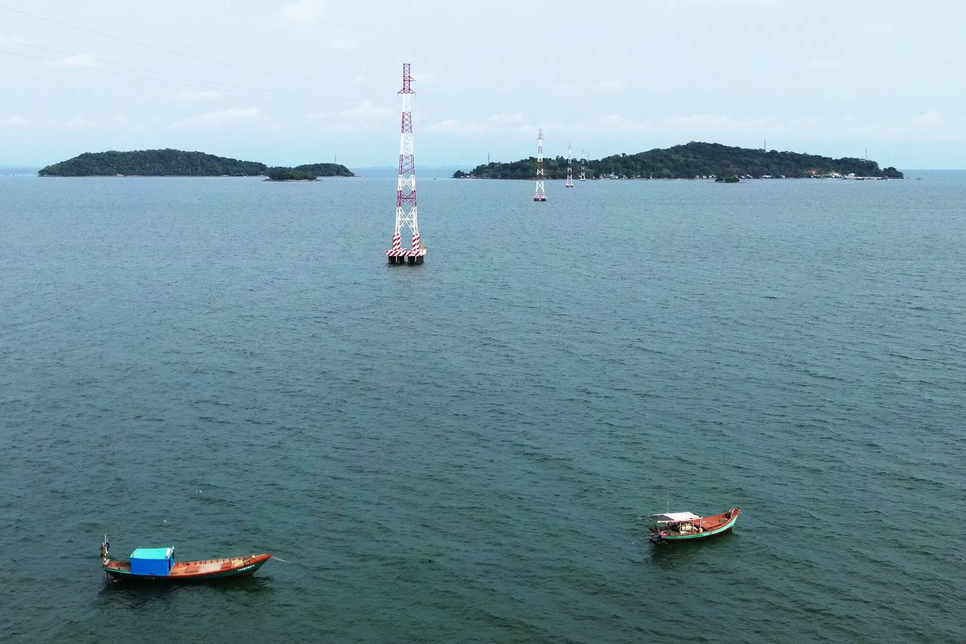 Hai tàu cá neo giữa biển, phía xa là trụ điện vượt biển và các hòn đảo nhỏ của quần đảo Hải Tặc